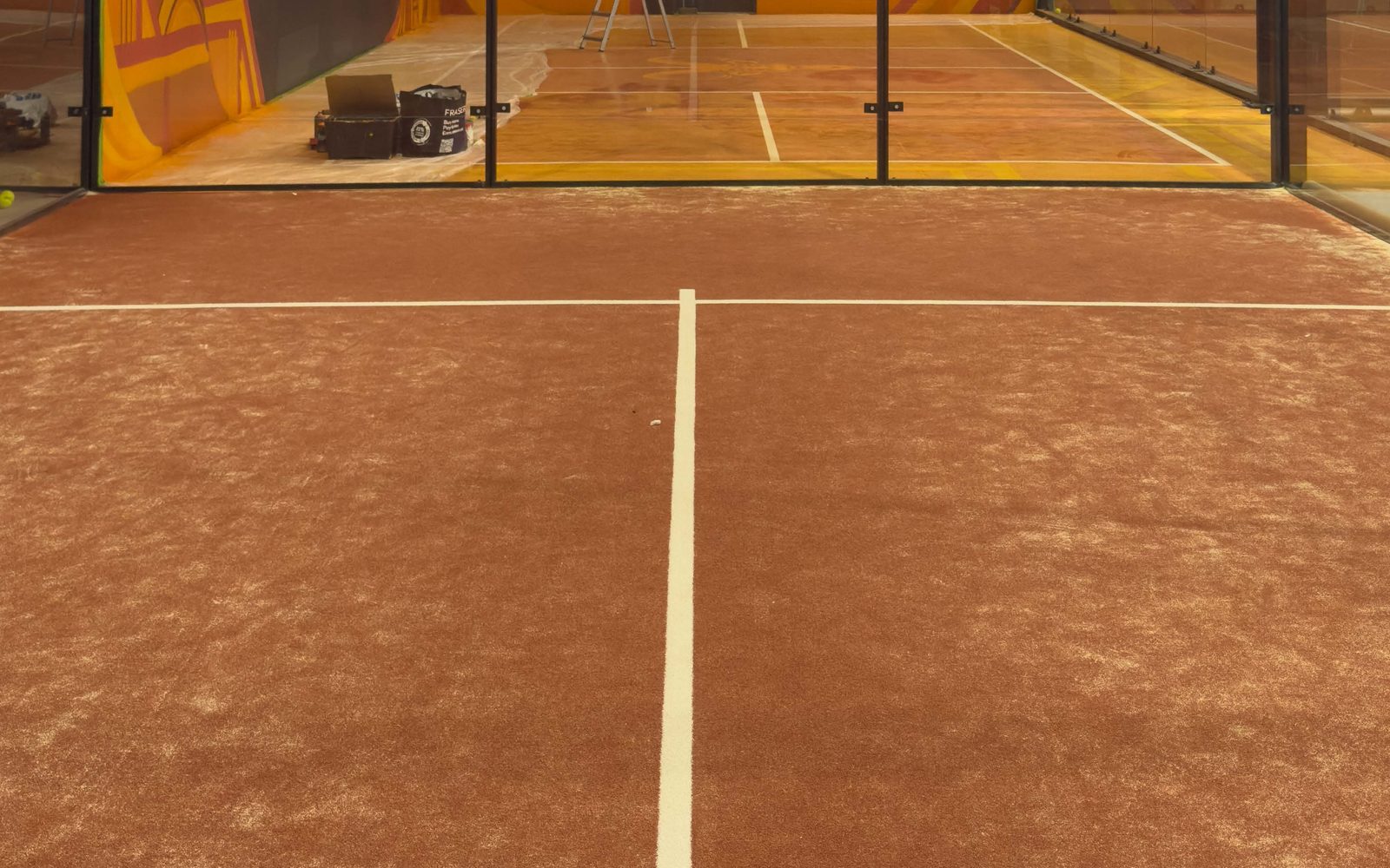 Padel court surface before maintenance, mottled with compacted dust and uneven sand